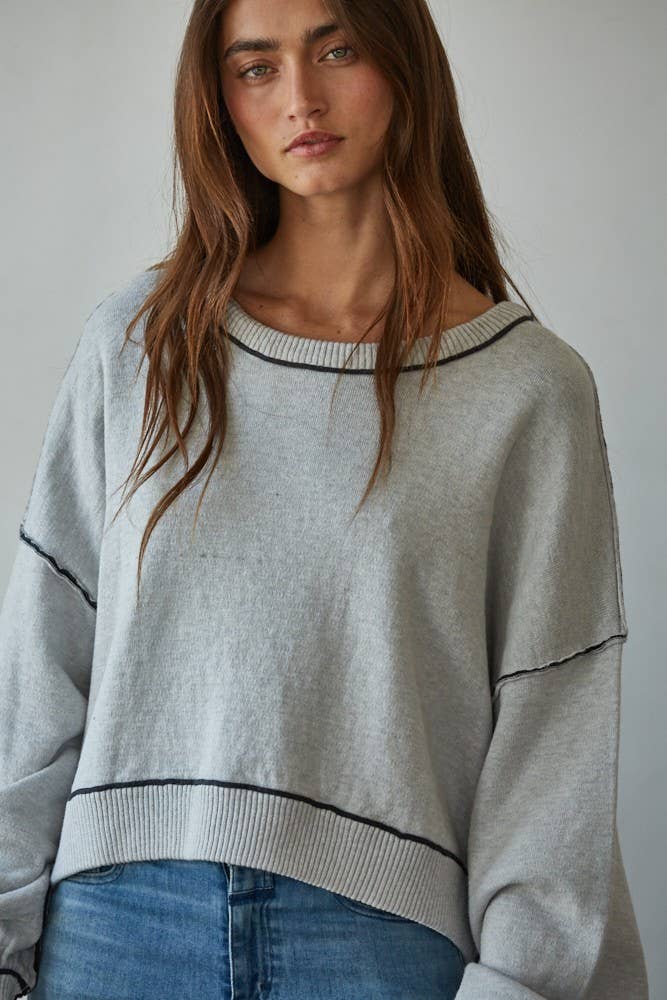 Woman wearing a light gray sweater with dark trim against a plain background