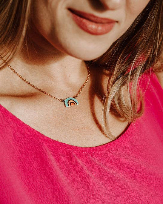 Person wearing a pink sleeveless top and a necklace with a rainbow pendant.