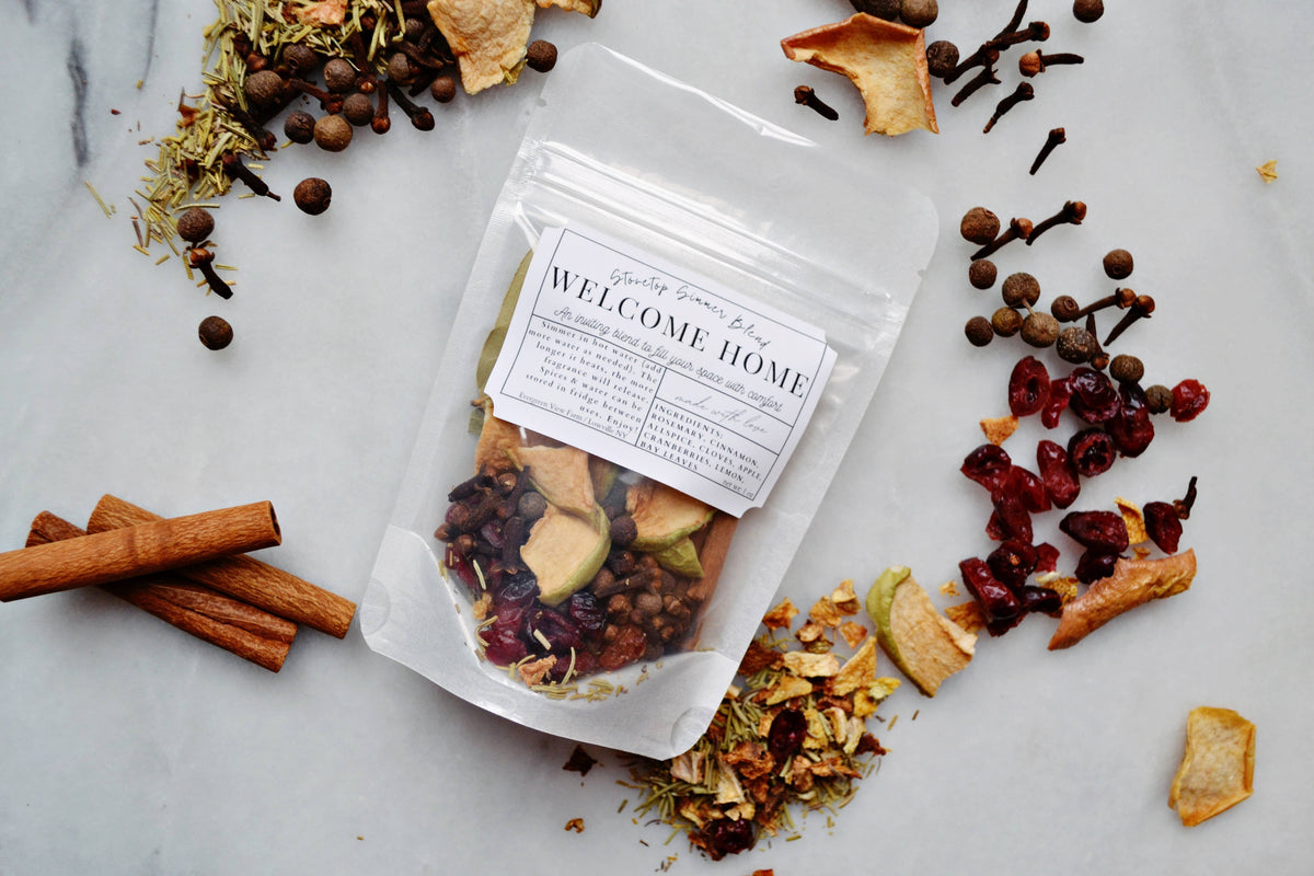 Tea bag labeled 'Welcome Home' surrounded by dried herbs and spices on a marble surface