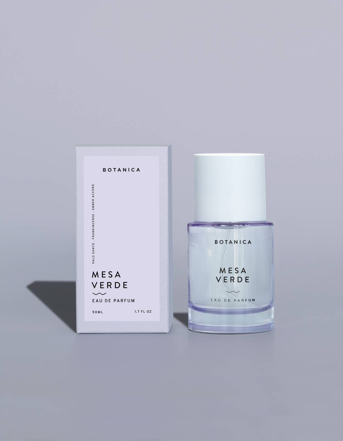A clear glass bottle of Botanica Mesa Verde Eau de Parfum with a white cap, standing next to its white packaging box on a light gray background.