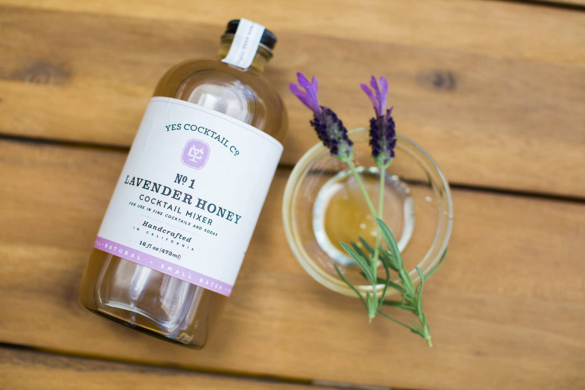 Bottle of Lavender Honey cocktail mixer with a sprig of lavender on a wooden surface