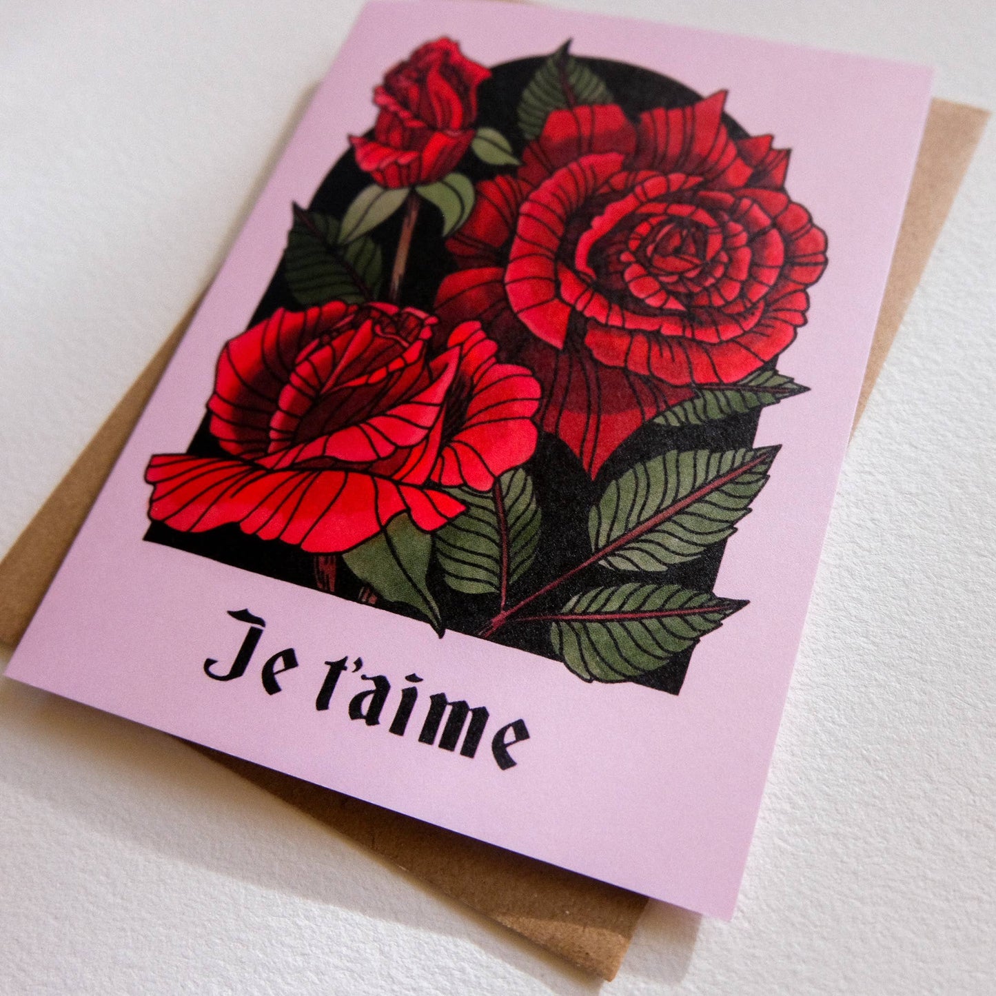 Greeting card with red roses and 'Je t'aime' text on a pink background