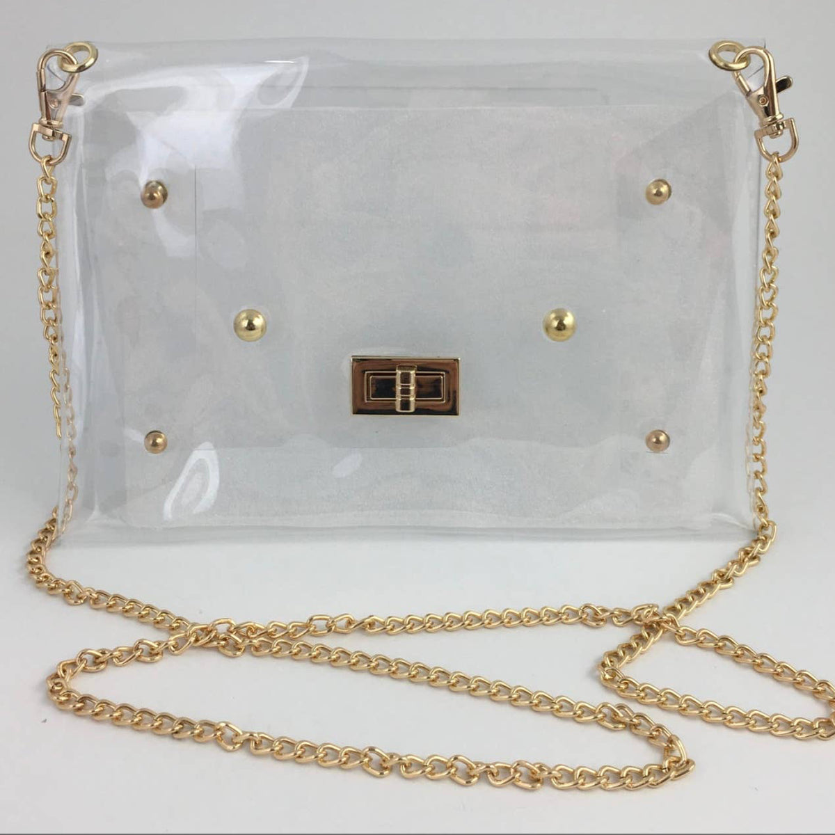 A clear vinyl shoulder bag with gold-tone hardware, including a chain strap, gold studs, and a central metal clasp, shown on a plain light background.