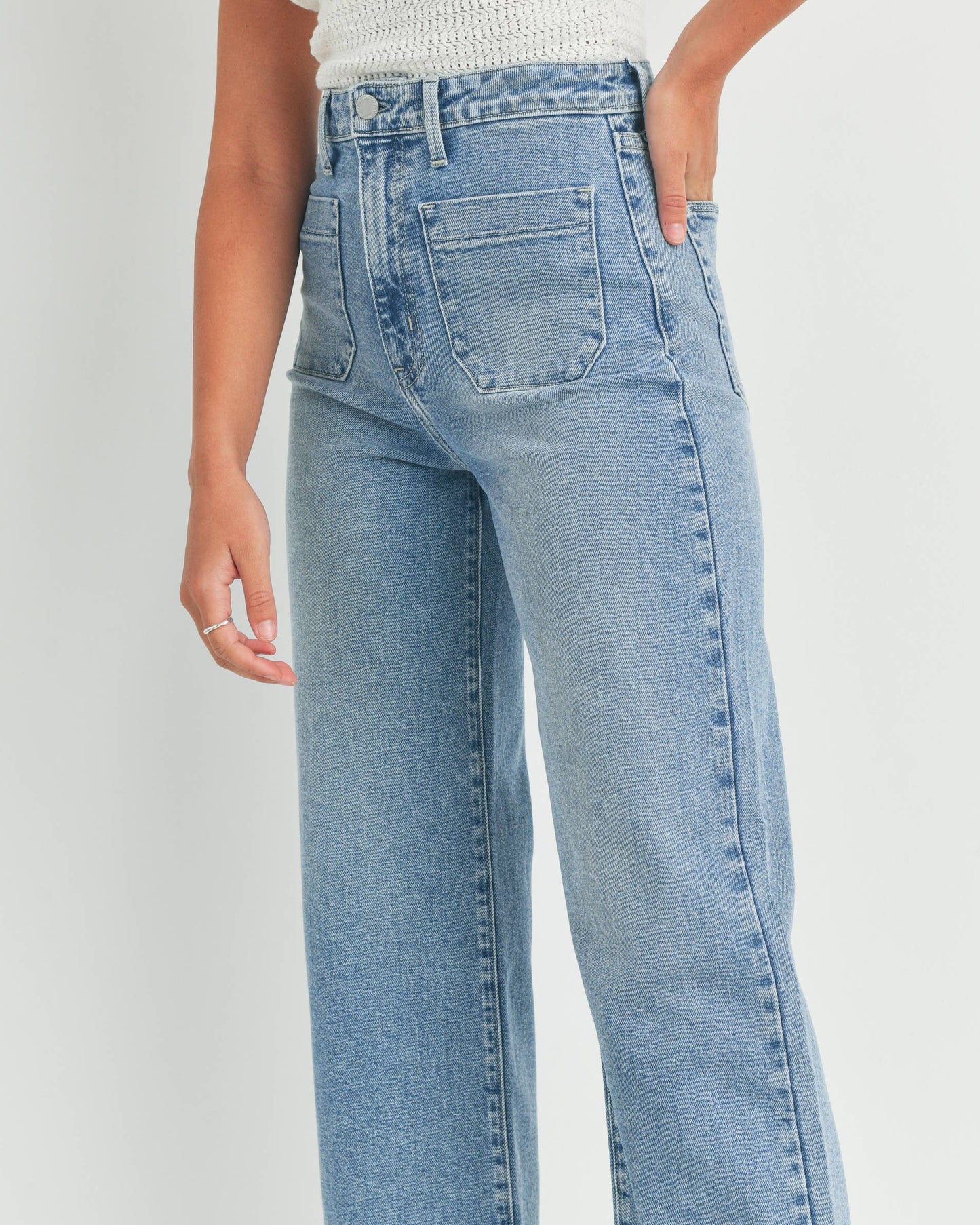 Person wearing light blue jeans and a white top against a plain background