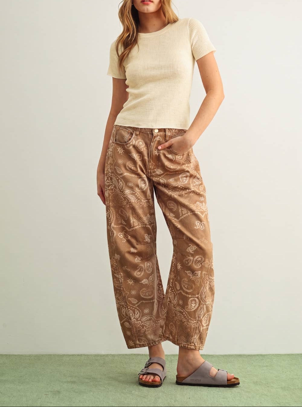 Woman wearing a beige top and patterned brown pants on a light green background