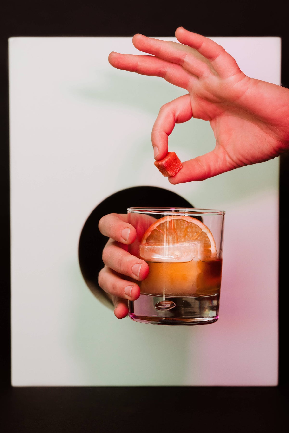 Hand holding a glass of cocktail with an orange slice against a blurred background
