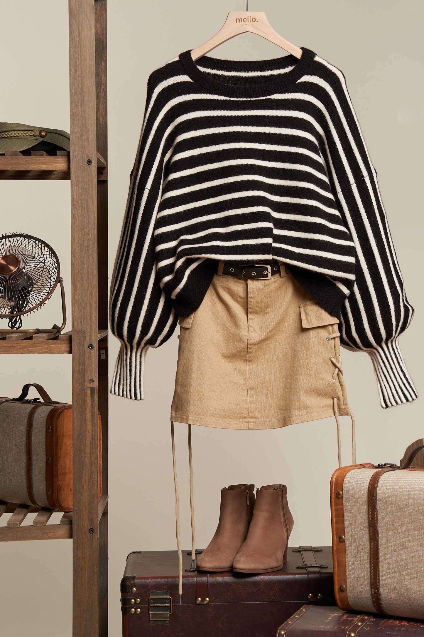 Black and white striped sweater with beige shorts and brown boots on a hanger against a neutral background.