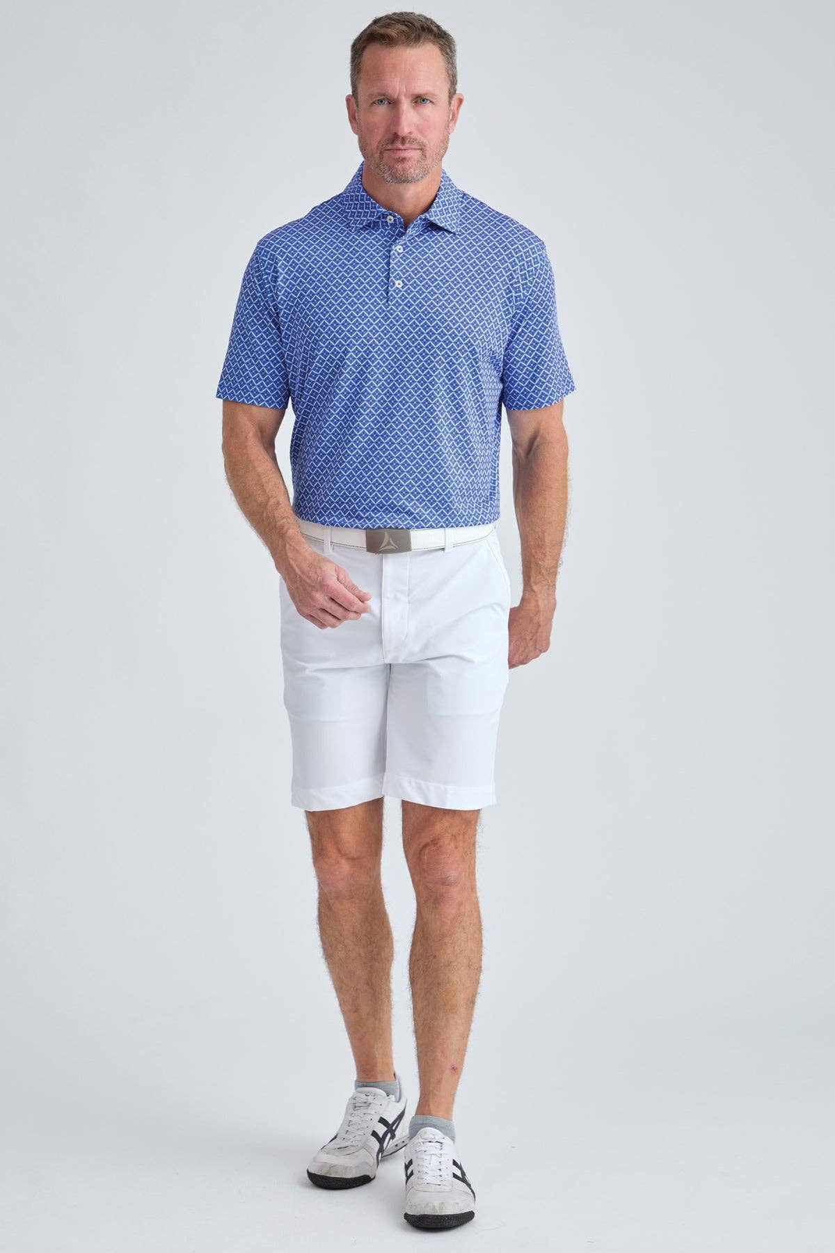 Man wearing a blue patterned polo shirt and white shorts on a light gray background