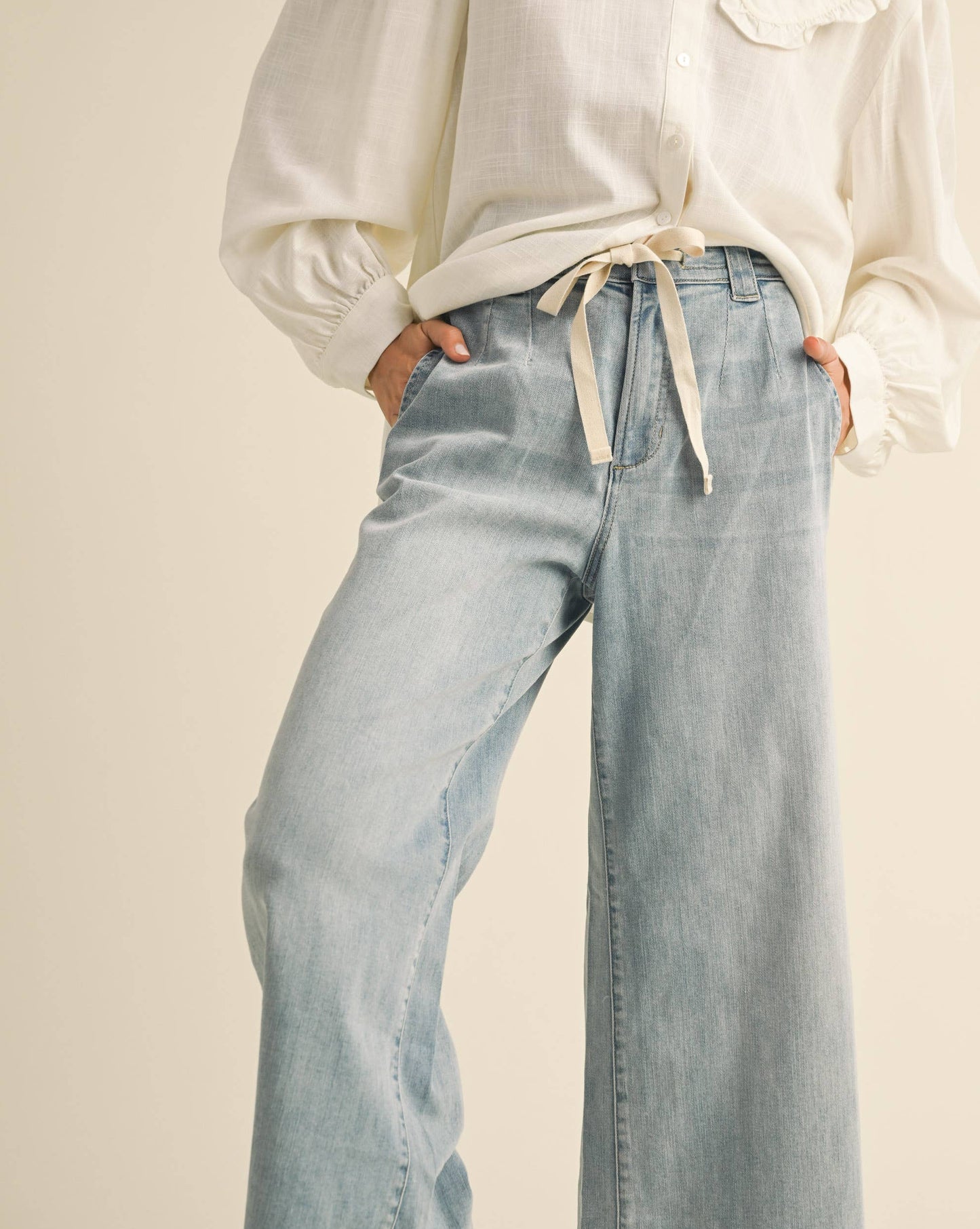 Person wearing a white blouse with a ruffled collar and light blue jeans on a beige background