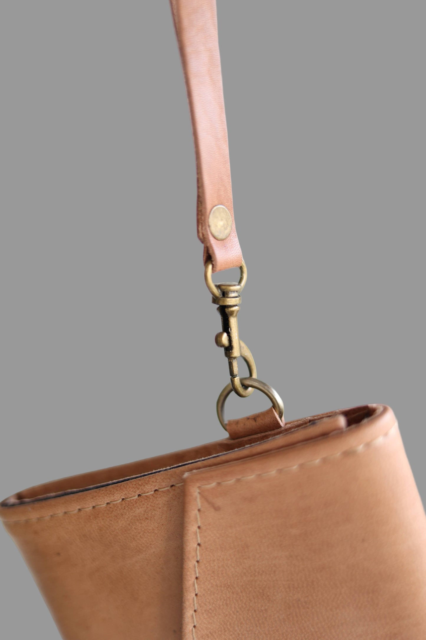 Close-up of a brown leather handbag with a strap and brass clasp on a light background