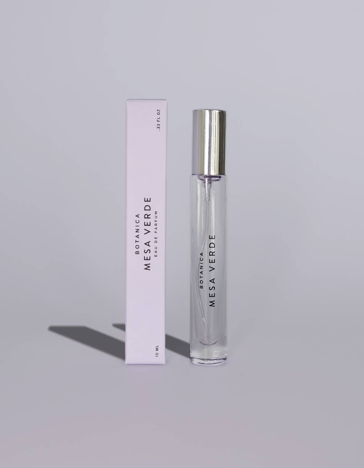 A clear glass rollerball perfume bottle with a silver cap stands next to its pale pink rectangular box. The box and bottle are printed with the brand name 'MESA VERDE' and scent name 'SEMPER VIVO'.