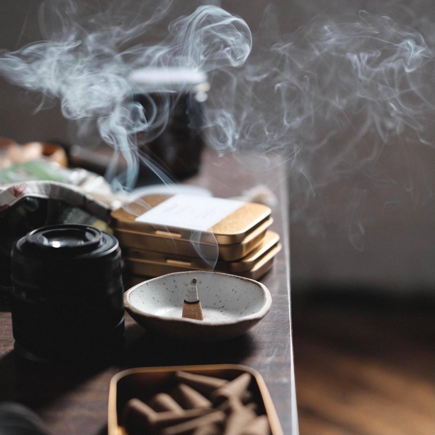 Incense burning in a small dish with smoke rising, on a wooden surface.