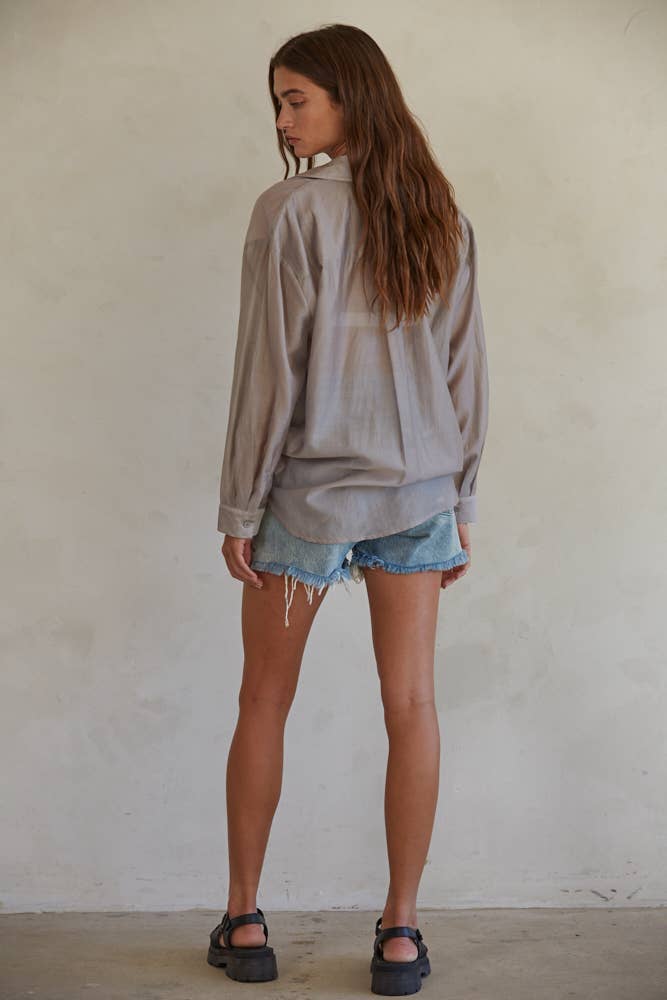 Woman wearing a light gray jacket and denim shorts against a plain wall.
