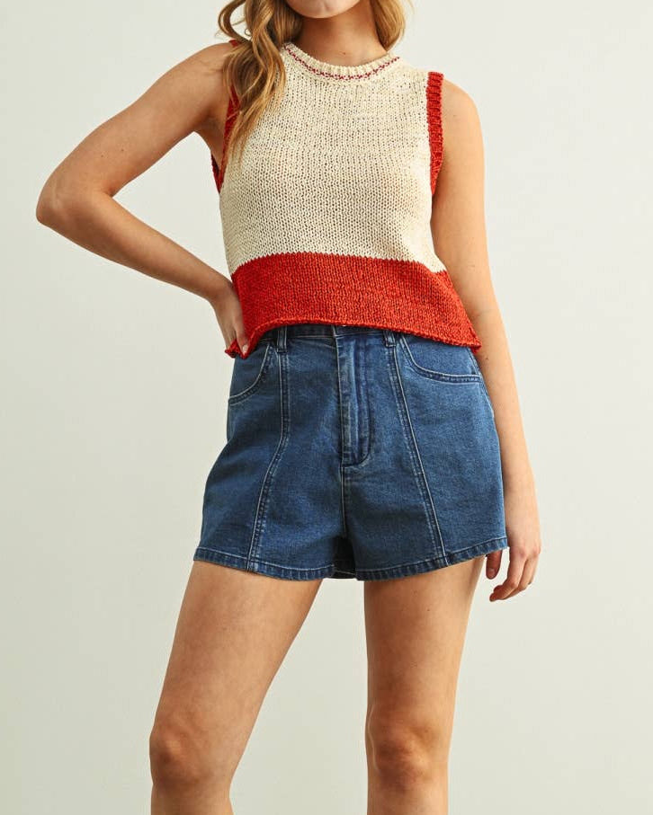 Woman wearing a red and beige sleeveless top with denim shorts on a light green background
