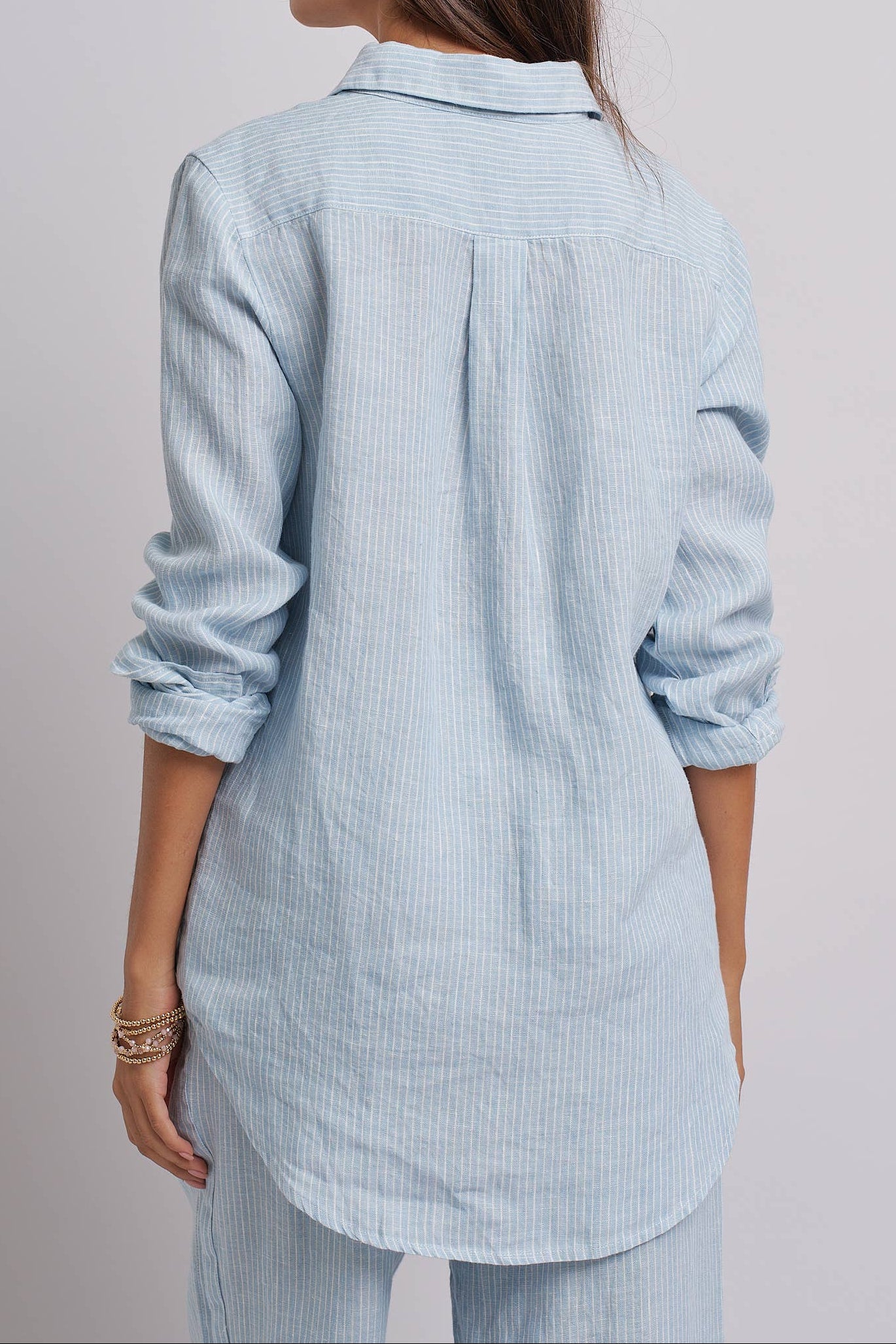 Woman wearing a light blue striped shirt against a plain background