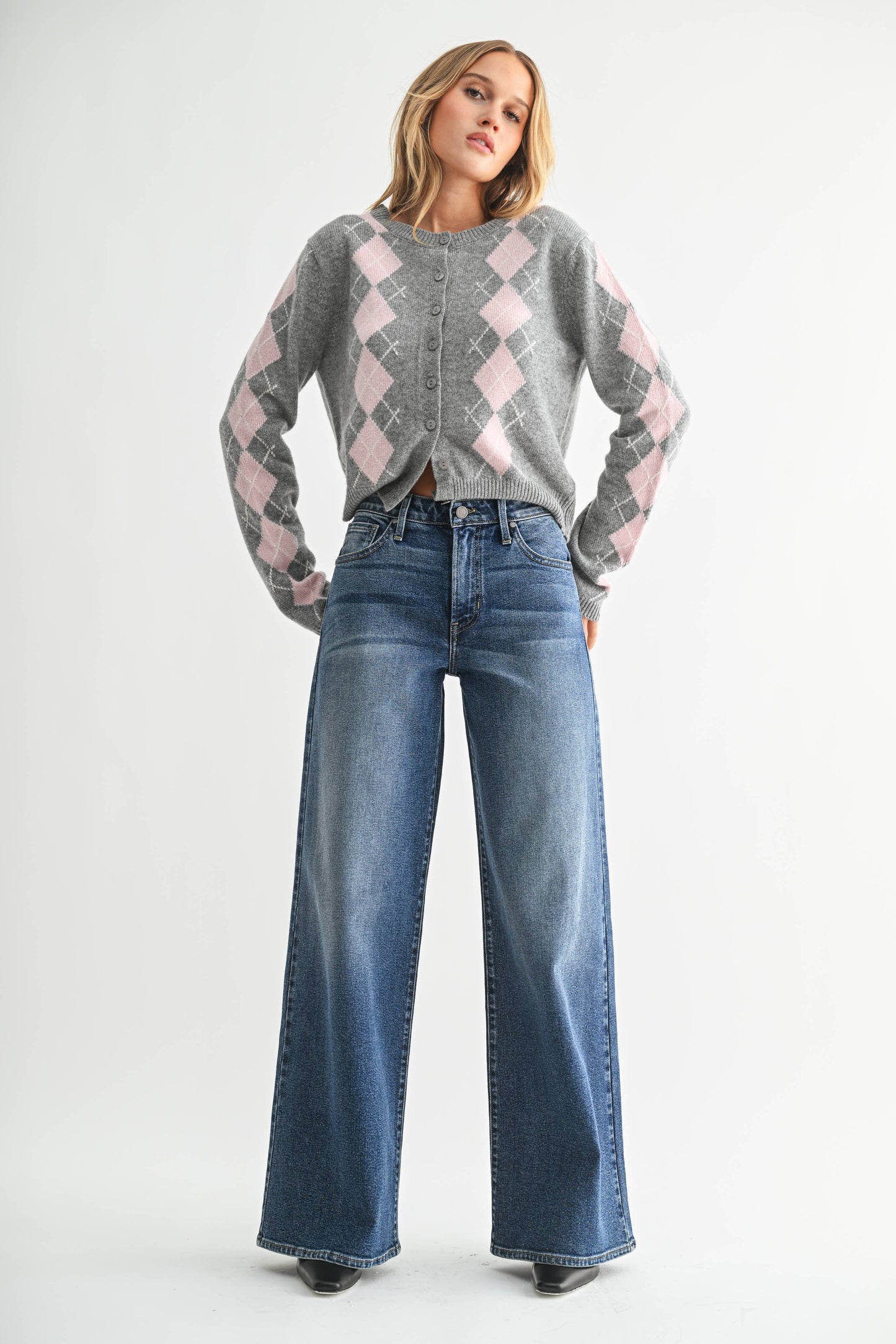 Woman wearing a gray and pink argyle sweater with wide-leg jeans on a white background