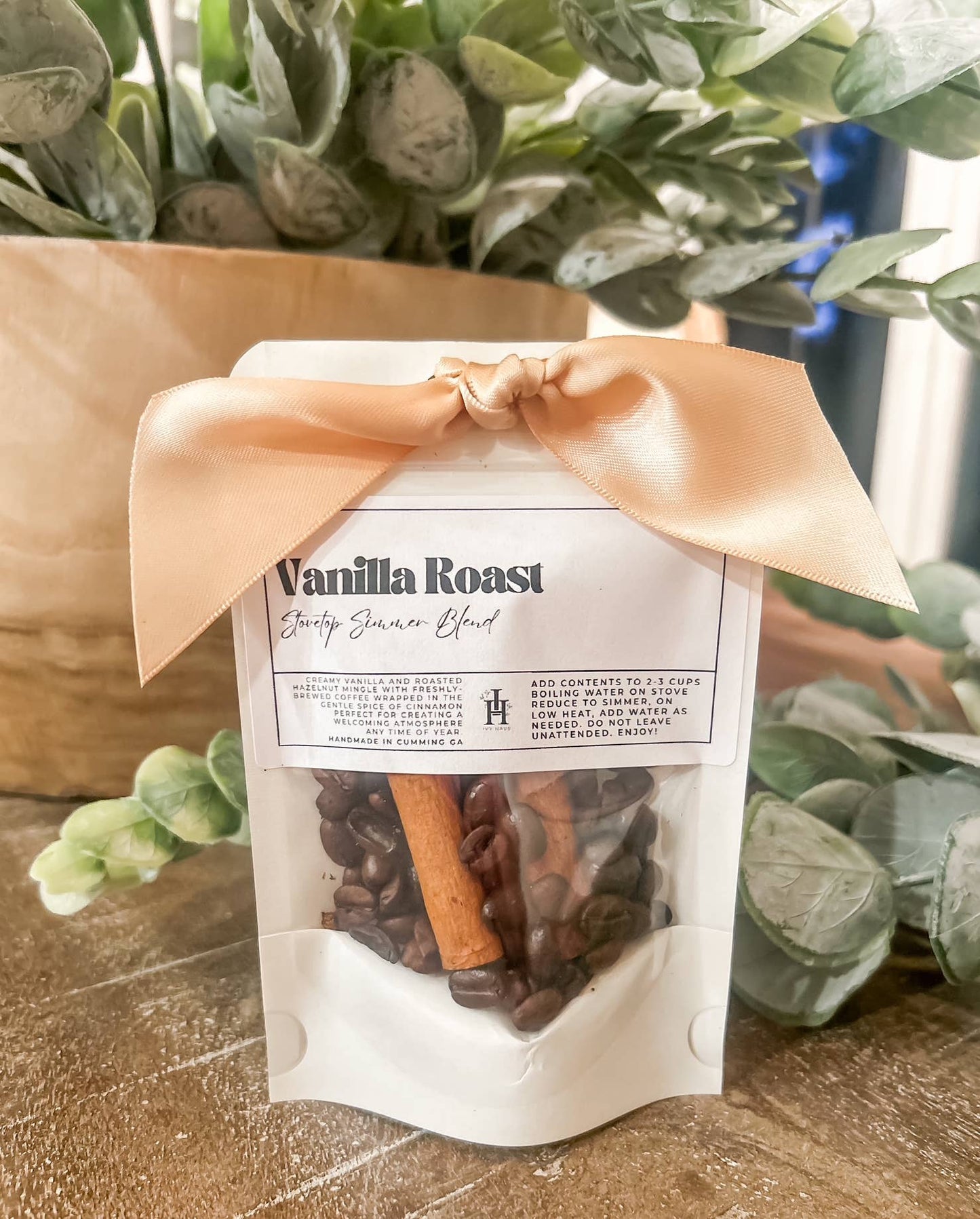 Packaged coffee blend with vanilla roast flavor, tied with a ribbon, on a wooden surface with greenery in the background.