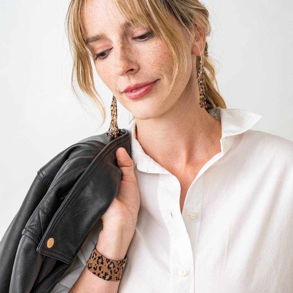 Woman wearing a white shirt and black jacket with gold earrings and bracelet on a light background