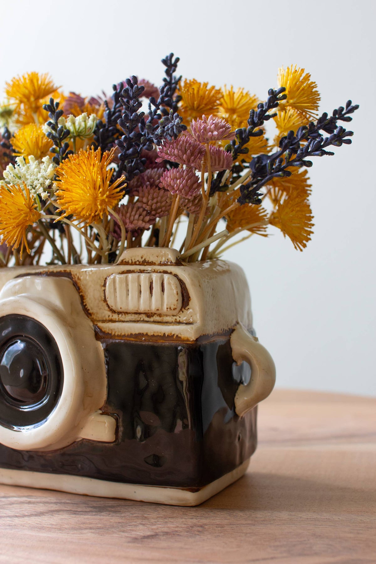 Ceramic camera-shaped vase with flowers on a wooden surface