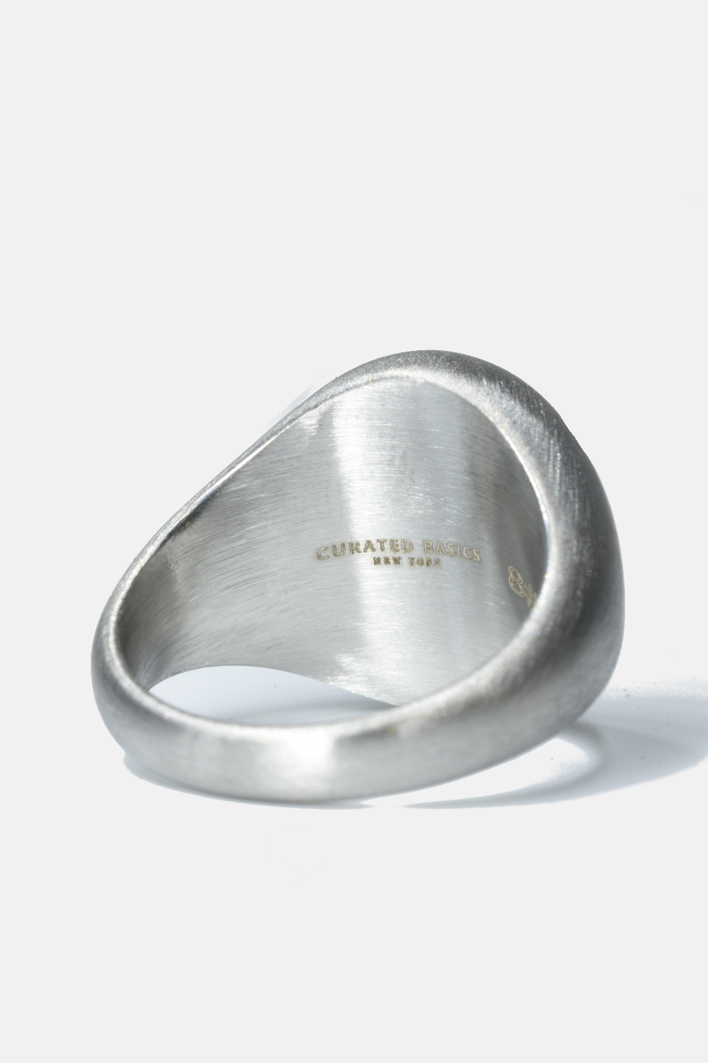 Silver ring with 'Curated Basics' engraving on a white background