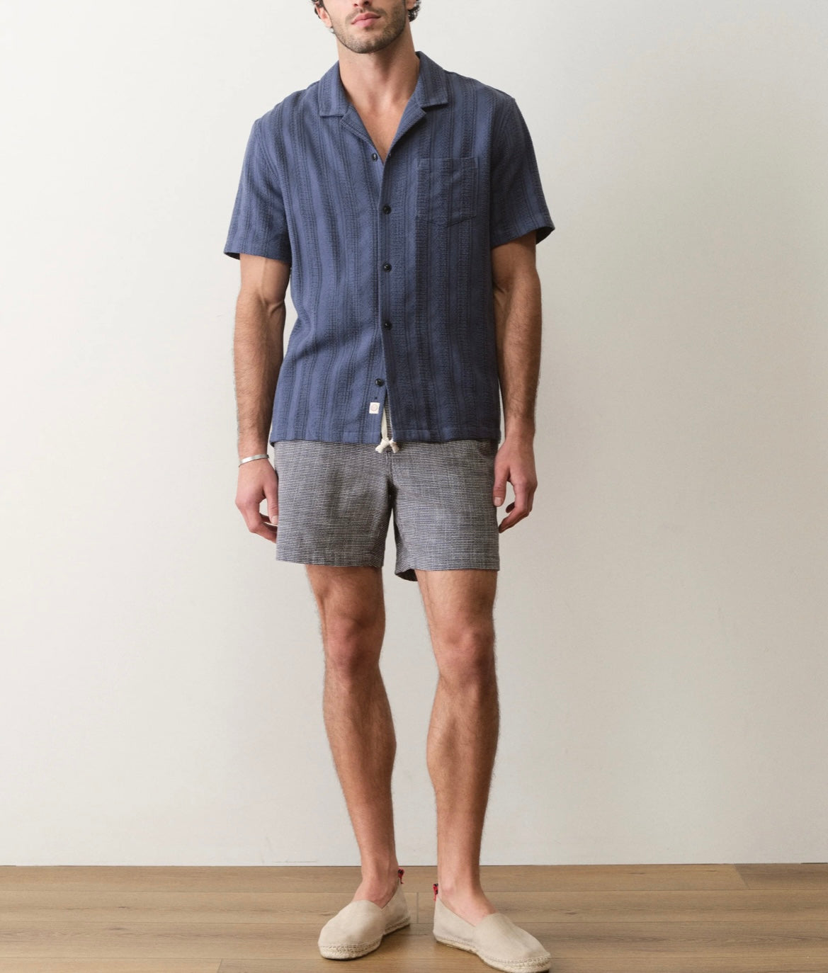 Man wearing a blue shirt and gray shorts against a plain background