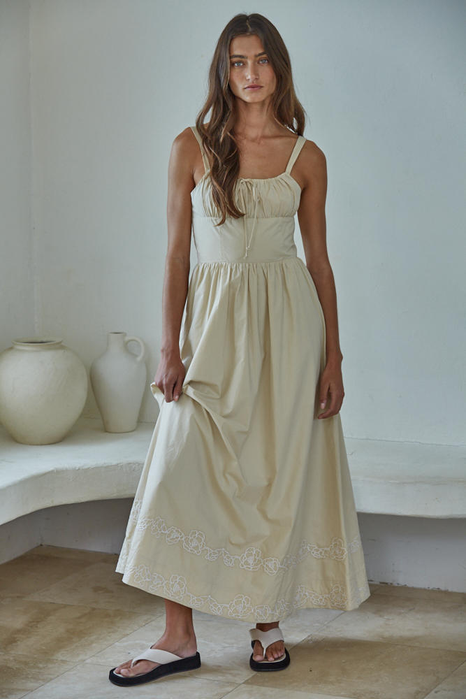 Woman wearing a light-colored dress standing in a minimalistic room with white walls and a shelf.