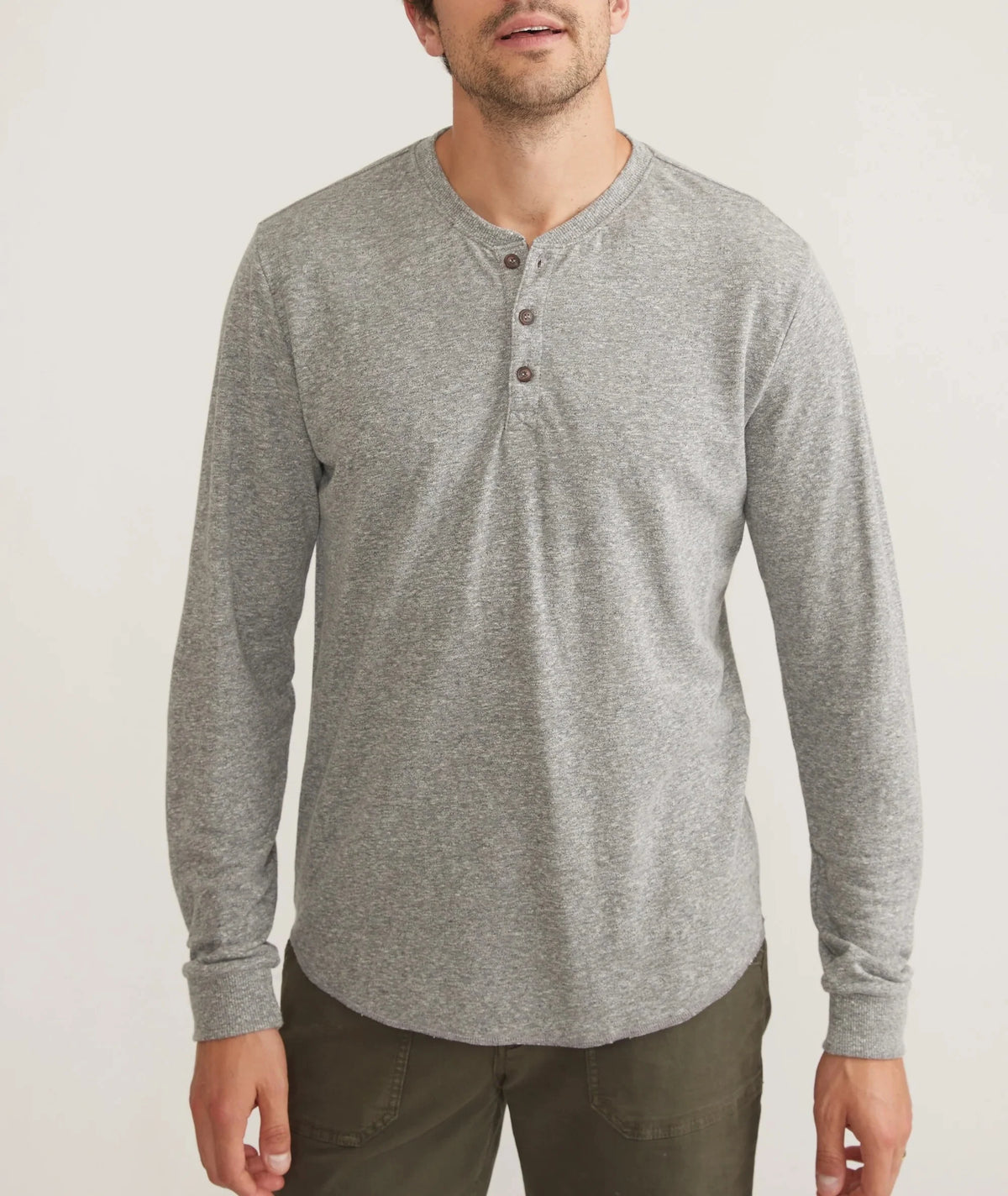 A man wearing a heather gray long-sleeve henley shirt with three buttons, paired with dark olive pants, against a plain light gray background.
