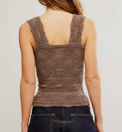 Rear view of a woman wearing a brown textured knit tank top with wide straps and a square neckline, paired with dark blue jeans against a plain light gray background.