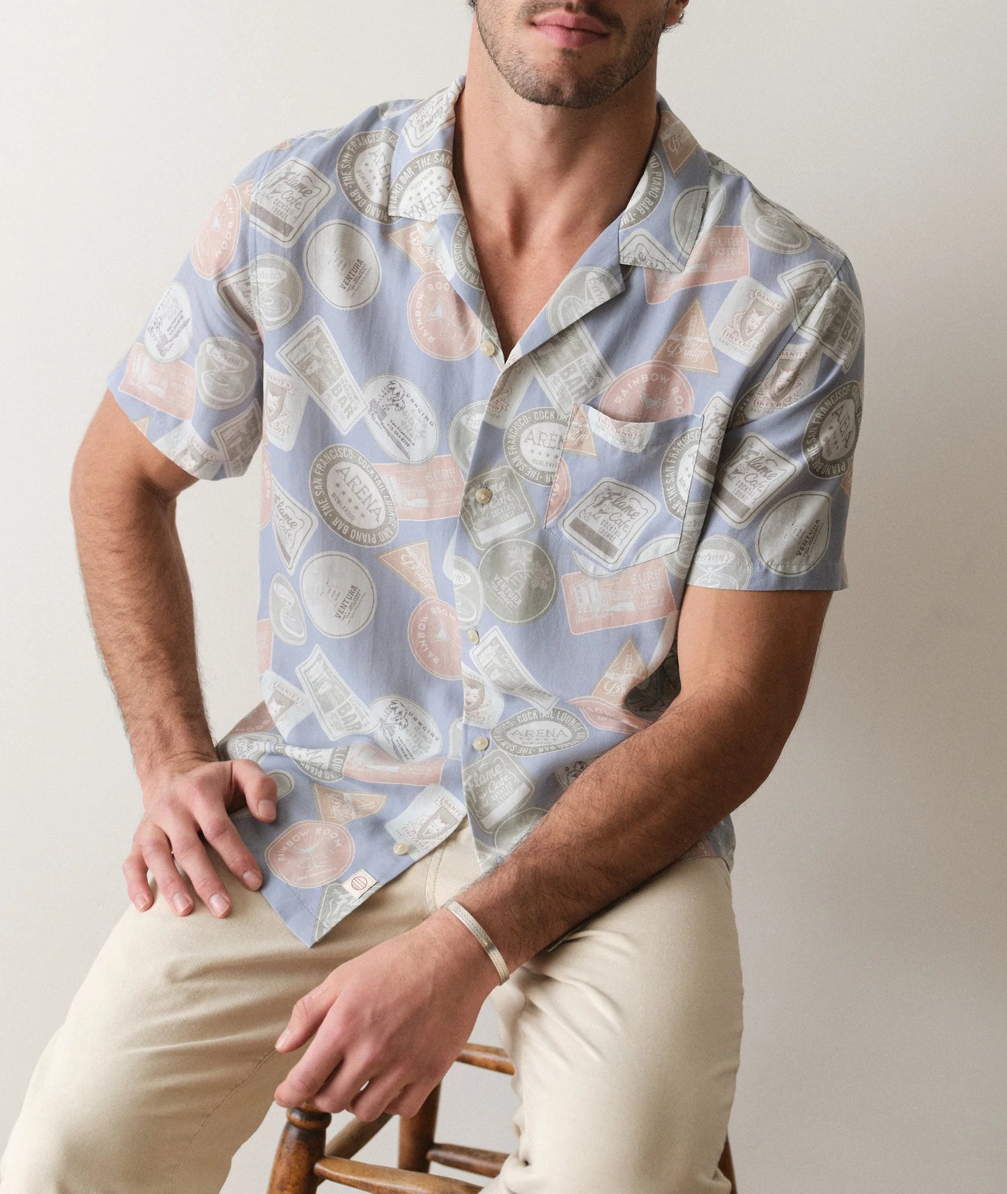 Man wearing a patterned shirt sitting on a chair against a plain background