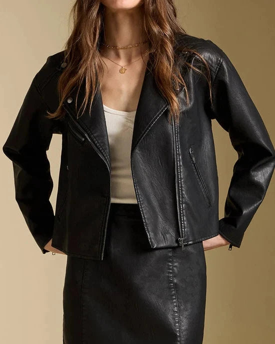 Woman wearing a black leather jacket and skirt against a beige background