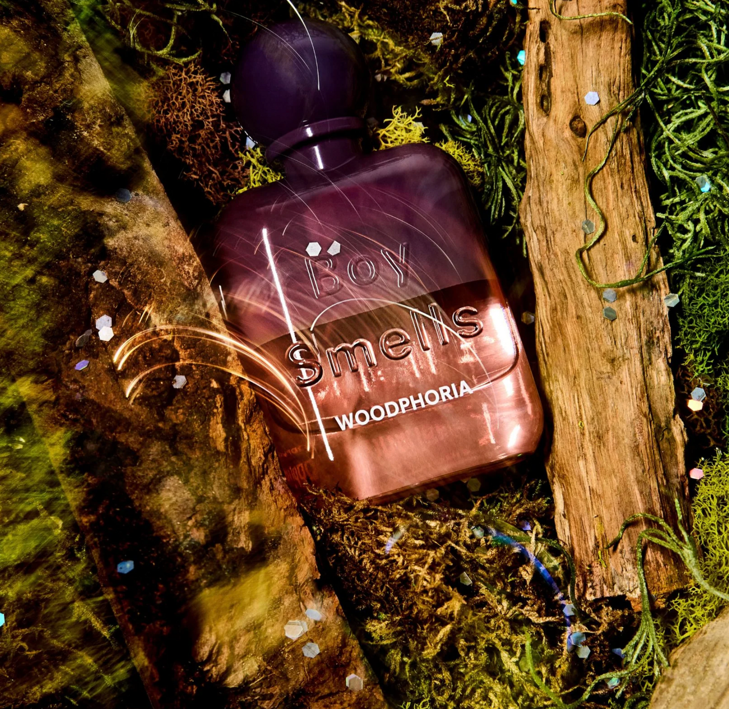 Perfume bottle labeled 'Boy Smells Woodphoria' on a natural background with moss and wood.