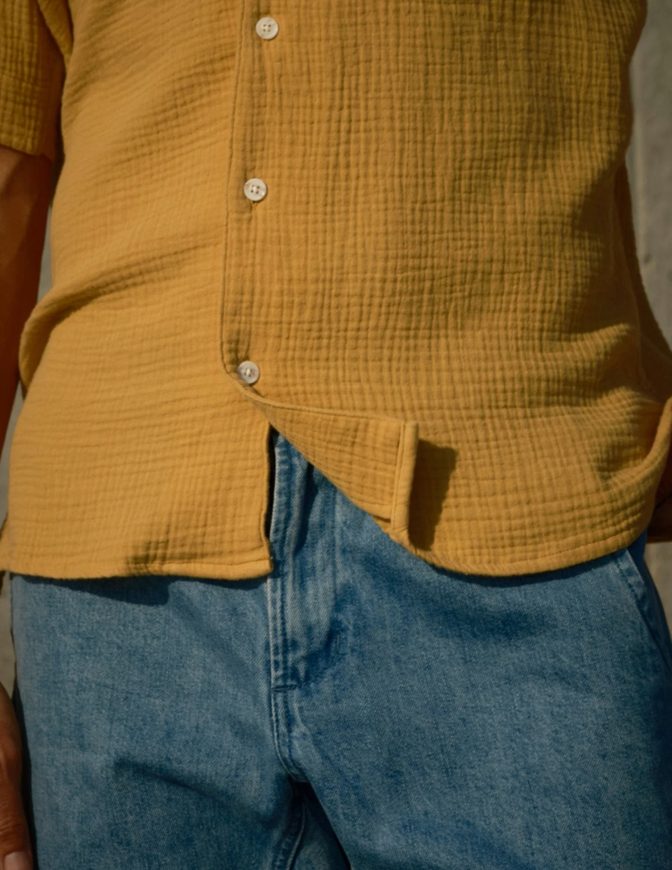 Person wearing a mustard yellow shirt and blue jeans with a blurred background