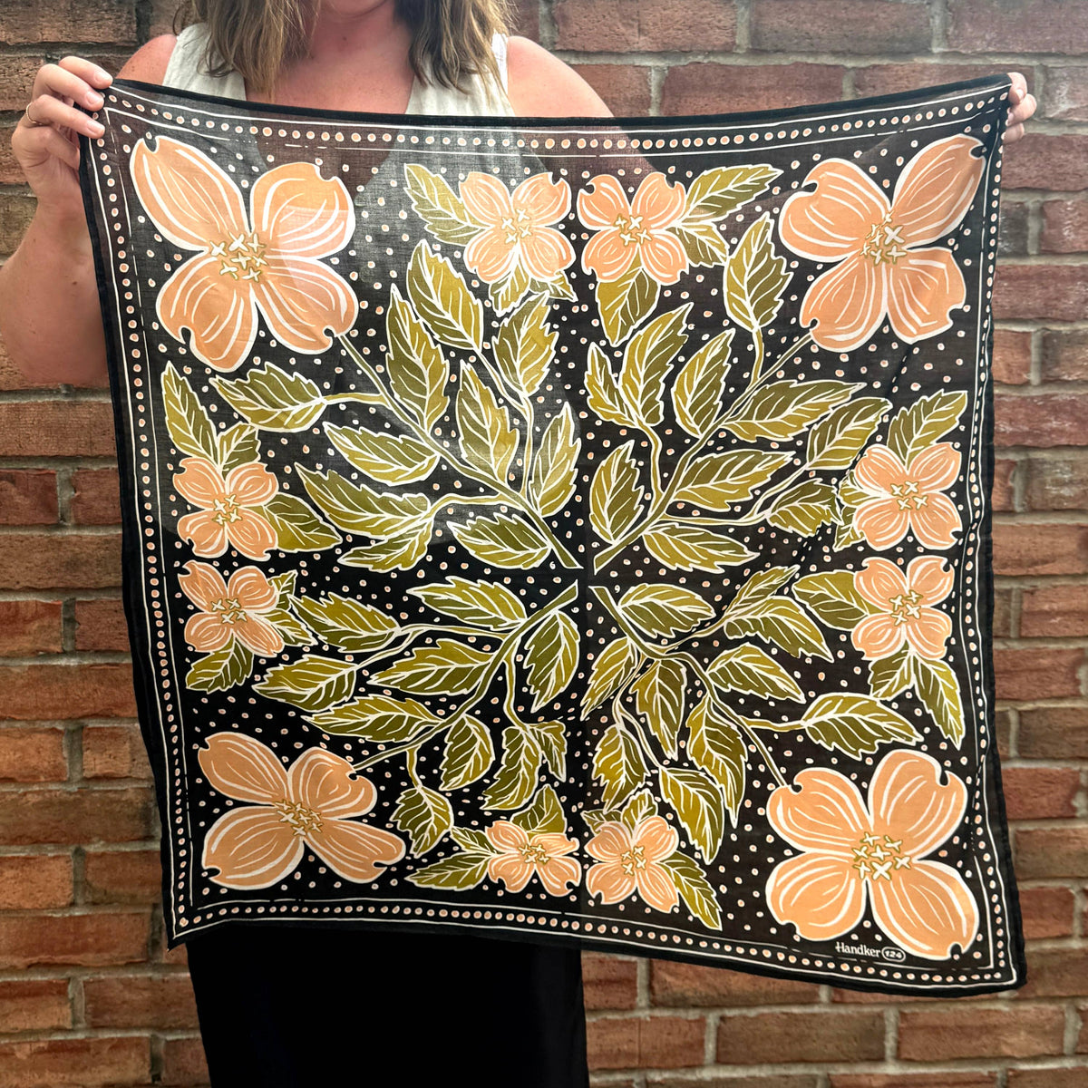 Person holding a floral patterned scarf against a brick wall