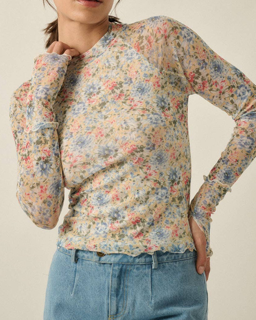 Woman wearing a floral long-sleeve top and blue jeans against a plain background