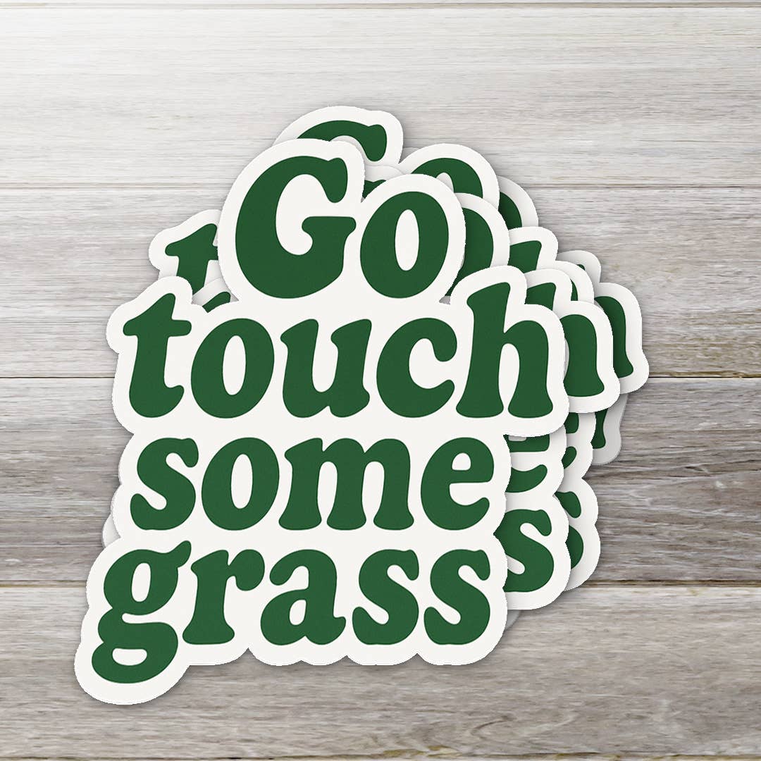 Stack of 'Go touch some grass' stickers on a wooden surface