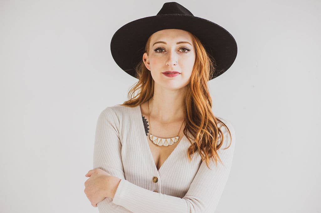 Woman wearing a black hat and beige cardigan on a white background