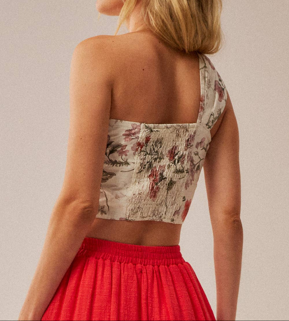 Woman wearing a floral top and red skirt against a plain background