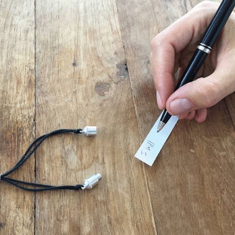 Hand holding a pen with a label next to two black cables on a wooden surface