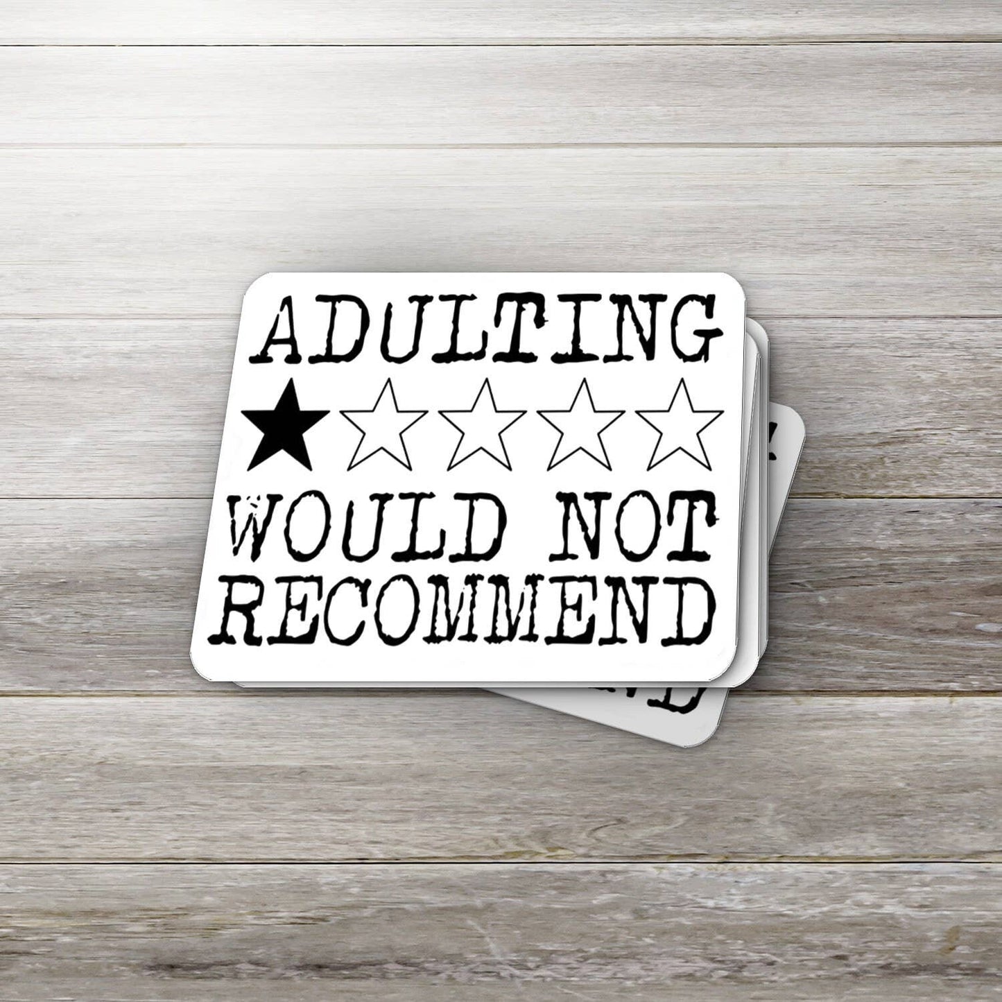 Stack of coasters with 'ADULTING WOULD NOT RECOMMEND' text and star ratings on a wooden surface