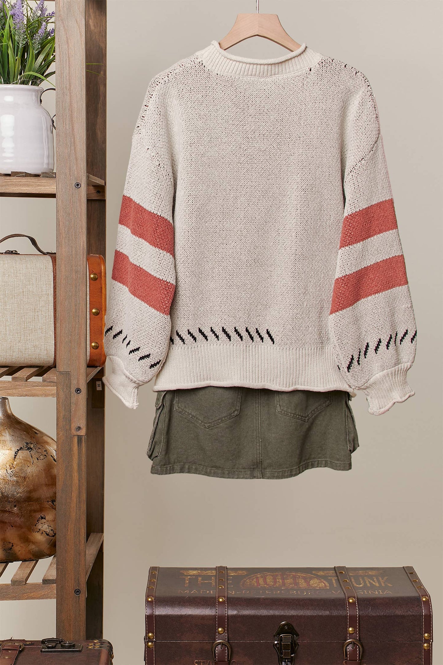 Beige sweater with red and black stripes on a hanger against a neutral wall.