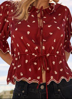 Woman wearing a red blouse with white patterns and a beige hat against a blue sky.