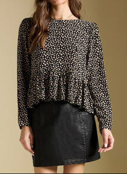 Woman wearing a patterned blouse and black skirt against a beige background
