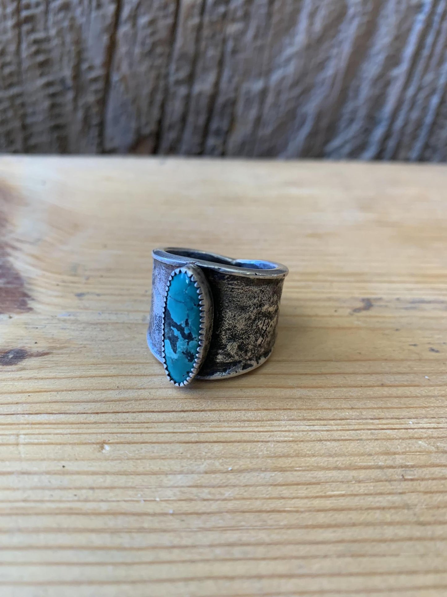 A hand forged sterling silver ring with a turquoise talon design on a wooden surface.