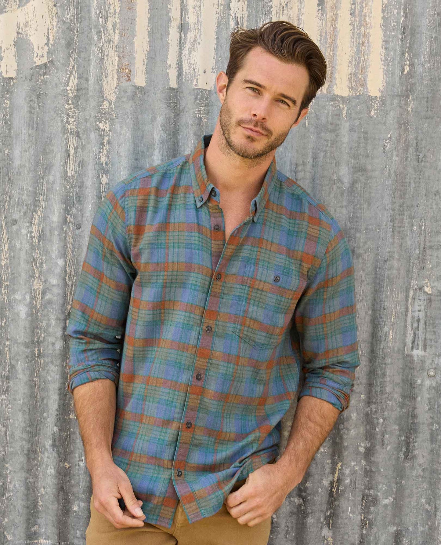 Man wearing a plaid shirt against a rustic wooden wall
