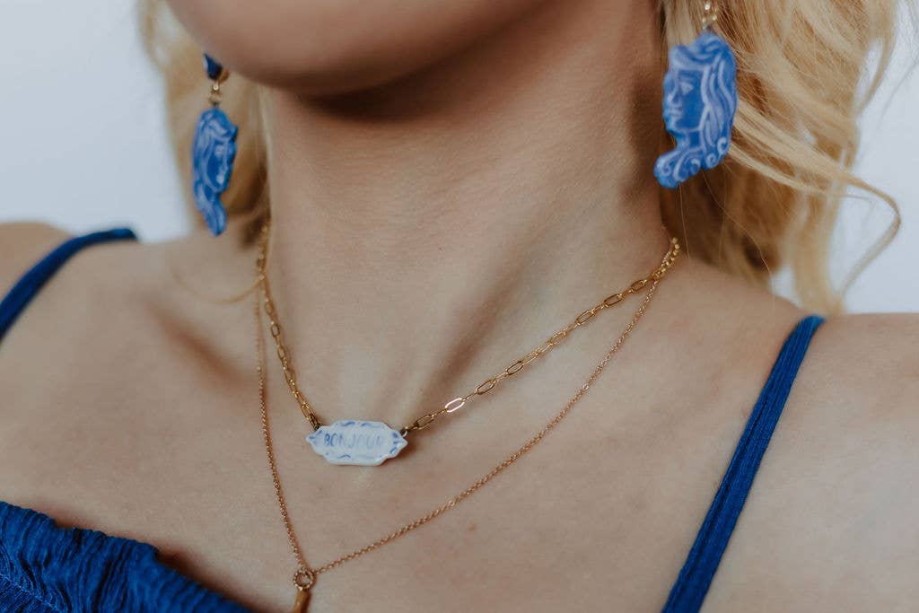 Close-up of a person wearing a gold necklace and blue earrings with a blurred background