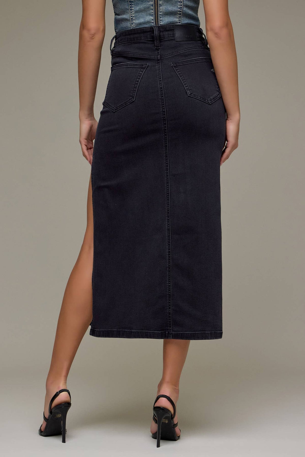 Person wearing a black denim skirt with a high slit on a neutral background