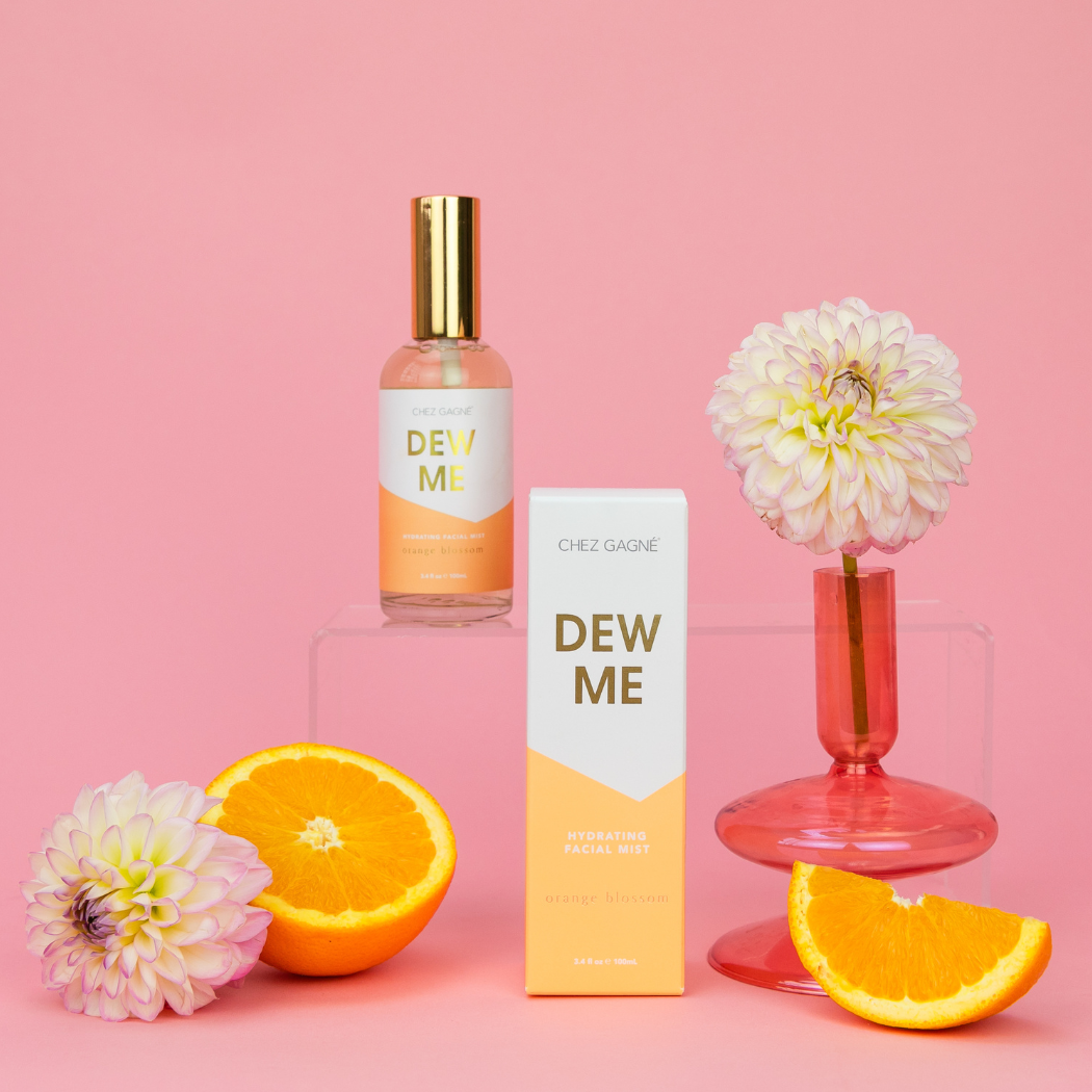 Chez Gagne Dew Me product with flowers and oranges on a pink background