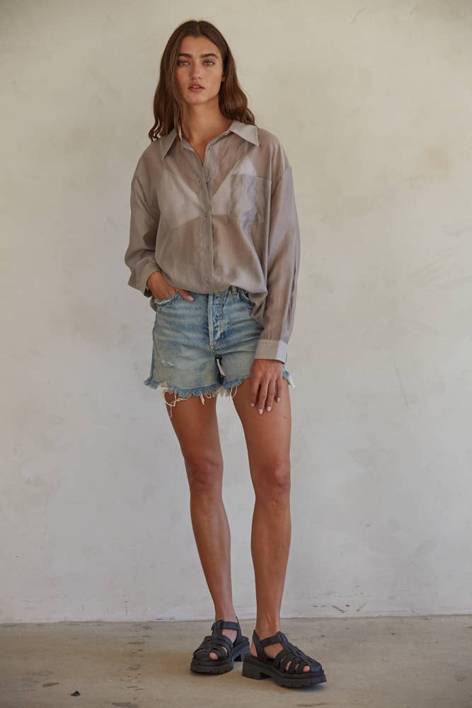 Woman wearing a light-colored shirt and denim shorts against a plain background