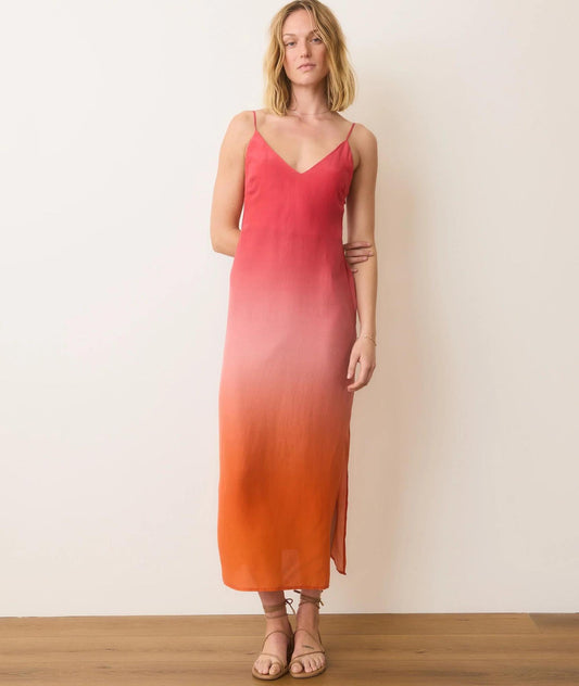 Woman wearing a pink to orange gradient slip dress against a white wall.