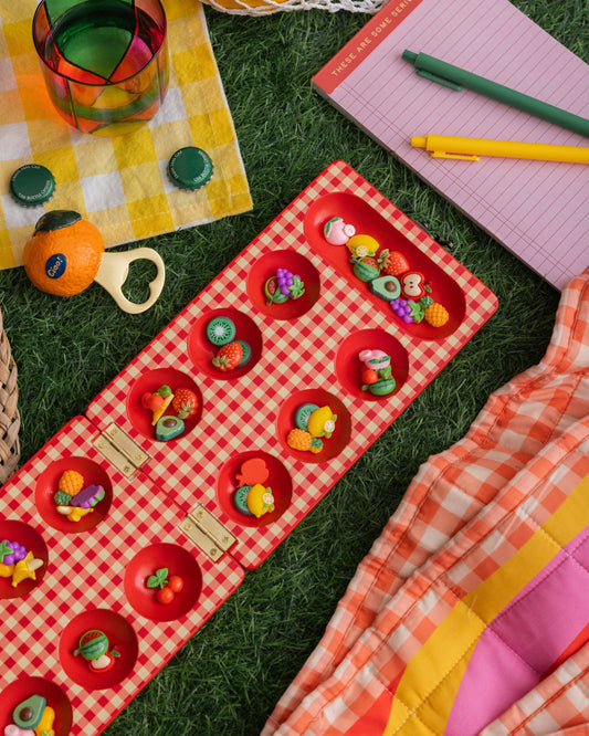 Colorful picnic setup with a red checkered blanket, toys, and stationery on grass.